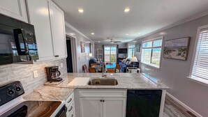 A kitchen with white cabinets, a built-in oven, a coffee maker, and a sink. - Inlet Point Villas #2A! Relax & Recharge in Cherry Grove’s Most Peaceful Corner (North Myrtle Beach)