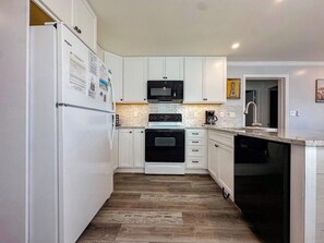 A kitchen with white cabinets, a black microwave, a stove, and a dishwasher. - Inlet Point Villas 2A (North Myrtle Beach)