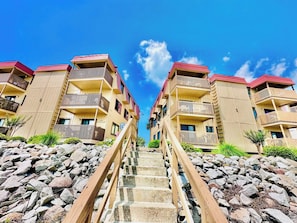 A hotel with a central staircase leading to multiple balconies, surrounded by a rocky landscape.