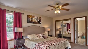 A bedroom with a bed, nightstands, a ceiling fan, a window with curtains, and a bathroom visible through an open door.