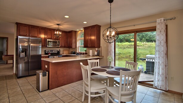 A modern kitchen with stainless steel appliances, wooden cabinets, and a dining area with white chairs.