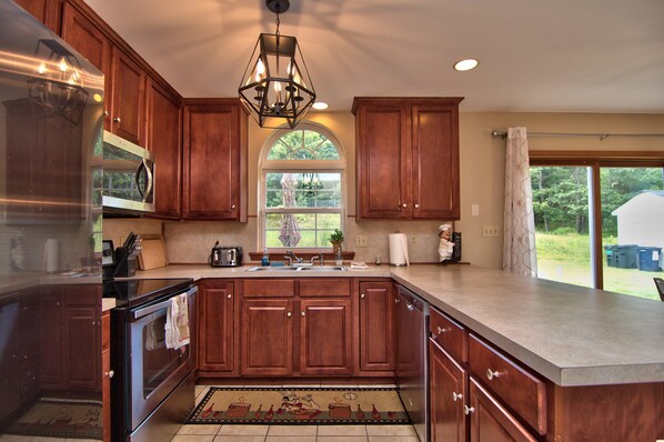 A kitchen with wooden cabinets, stainless steel appliances, a large window, and a view of the outdoors. - Luxury home, close to Kalahari, Ski Resorts, Fireplace, Ping Pong, Pool Table (Blakeslee)