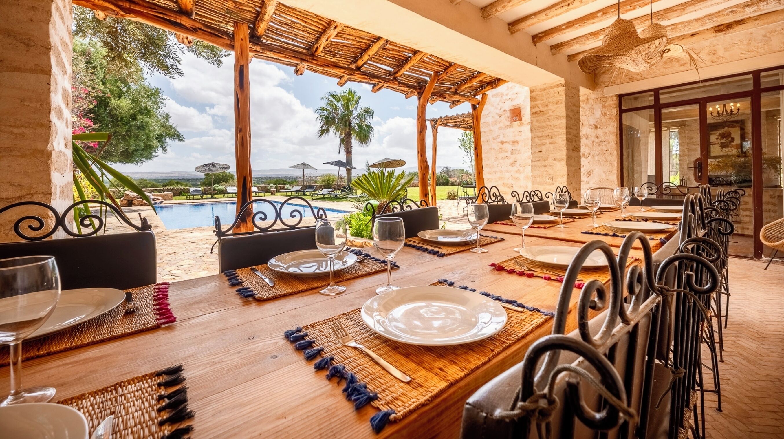 Ein Essbereich mit Blick auf den Pool, mit Holztischen, Metallstühlen und einer Pergola.