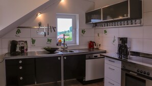 A modern kitchen with a black and white color scheme, featuring a built-in oven, a coffee maker, and a window providing natural light.