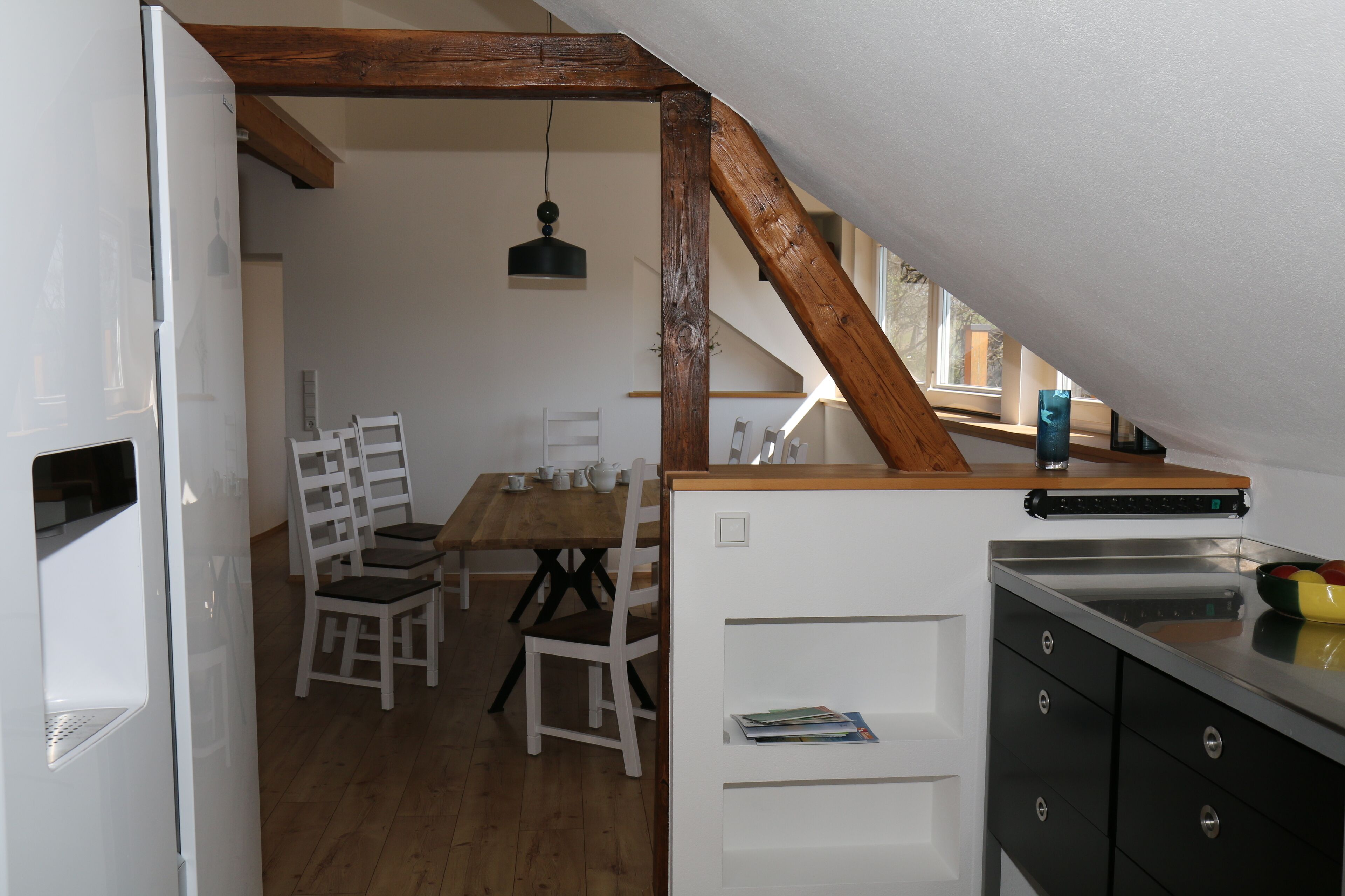 A kitchen with wooden beams, a dining table with chairs, and a refrigerator.