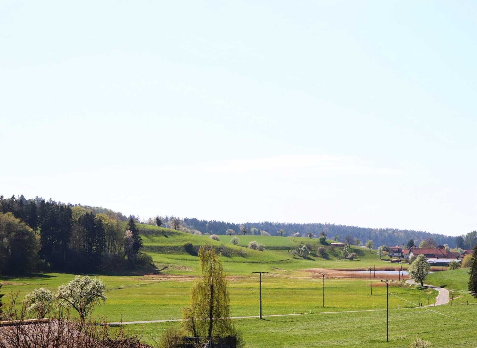 A rural landscape with rolling hills, a clear sky, and a few scattered buildings.