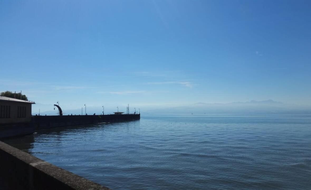 A waterfront view with a dock extending into calm water, a clear sky, and distant mountains.