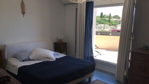 Une chambre à coucher avec un lit, une table de chevet, une commode et une fenêtre avec des rideaux.
