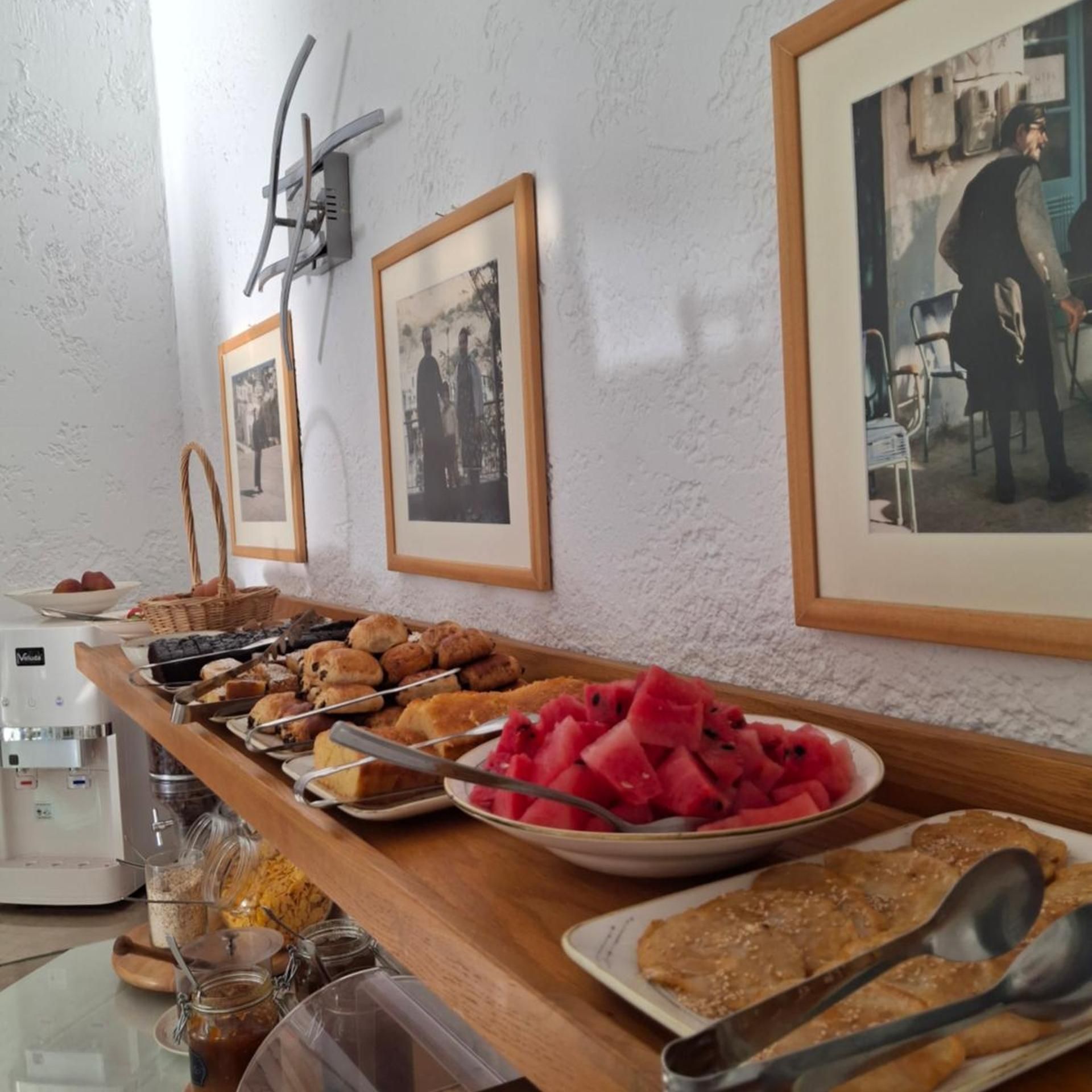 A breakfast buffet with various pastries, a bowl of watermelon, and a coffee machine.