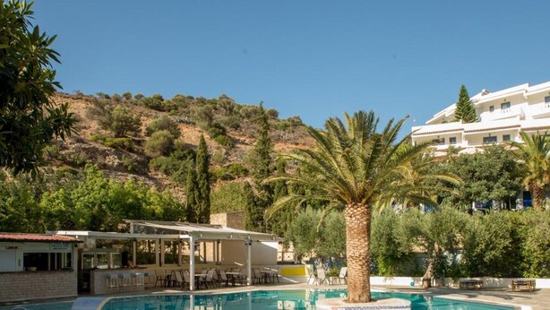 Una piscina con jacuzzi, zona de descanso y un paisaje con colinas al fondo.
