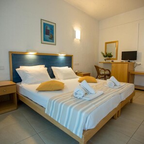 A hotel room with a double bed, a desk with a computer, a chair, and a painting on the wall. - Neos Ikaros (Agios Vasileios)