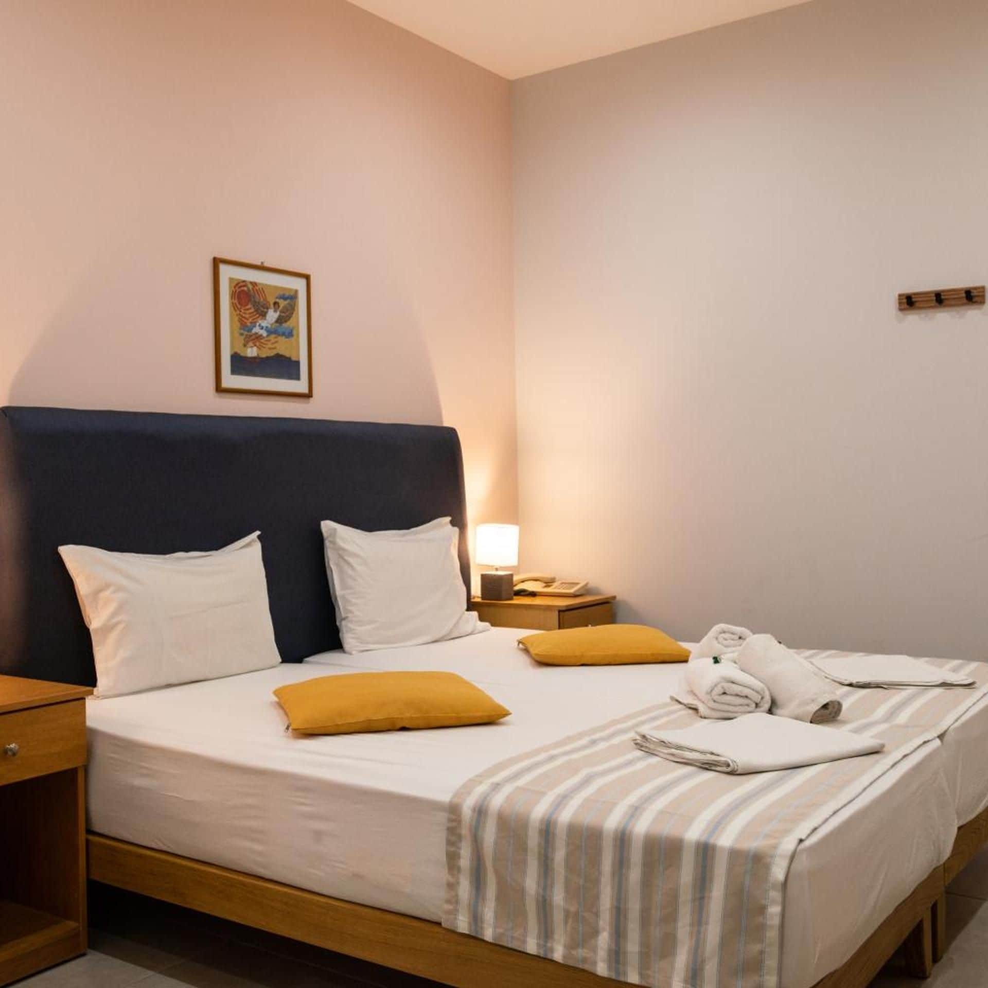 Et hotelværelse med en seng, to puder, et natbord med en lampe og et billede i ramme på væggen.