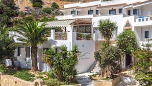 Un edificio blanco con una escalera que conduce a una entrada cubierta, rodeado de palmeras y plantas.