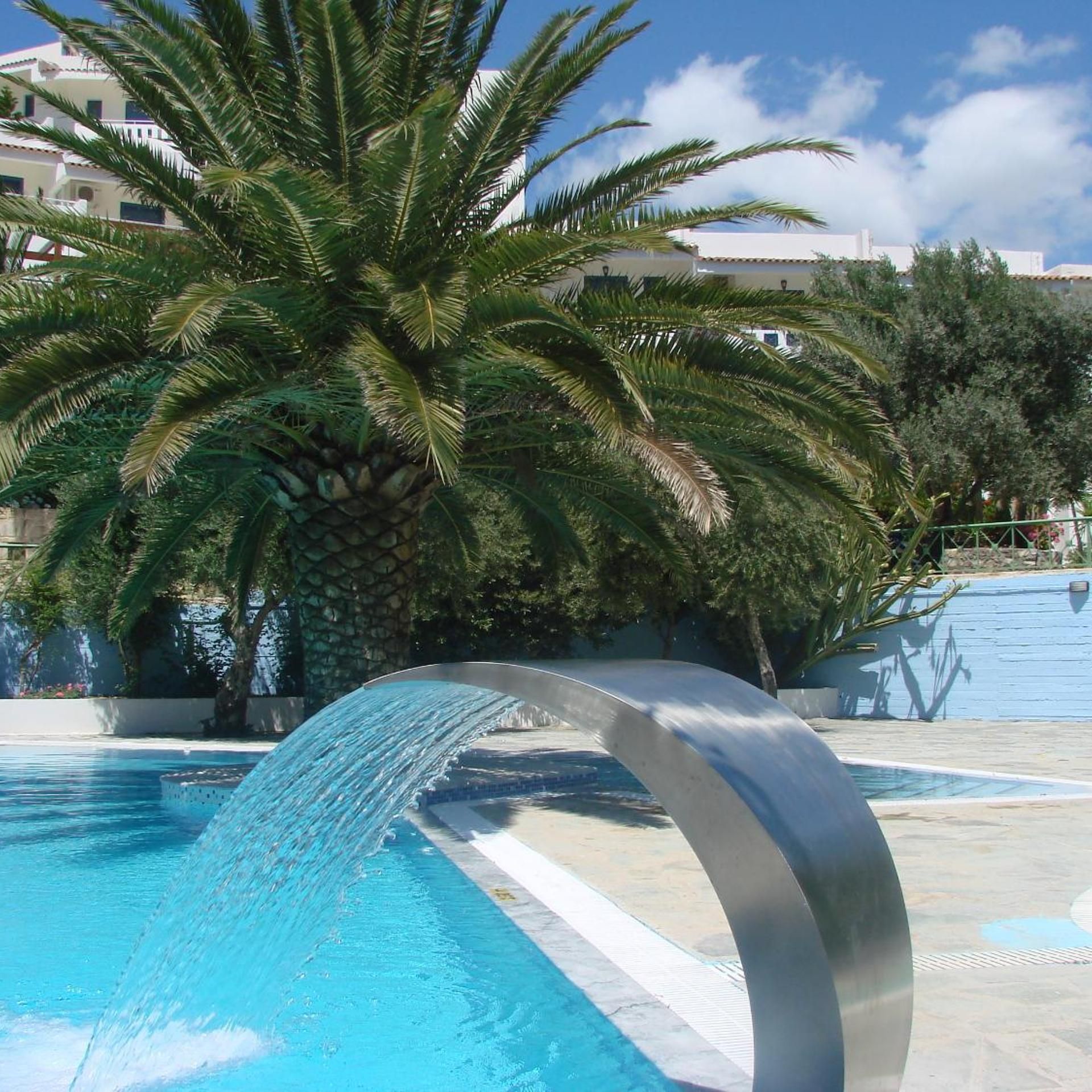 Una piscina con fuente, rodeada de palmeras y edificios.