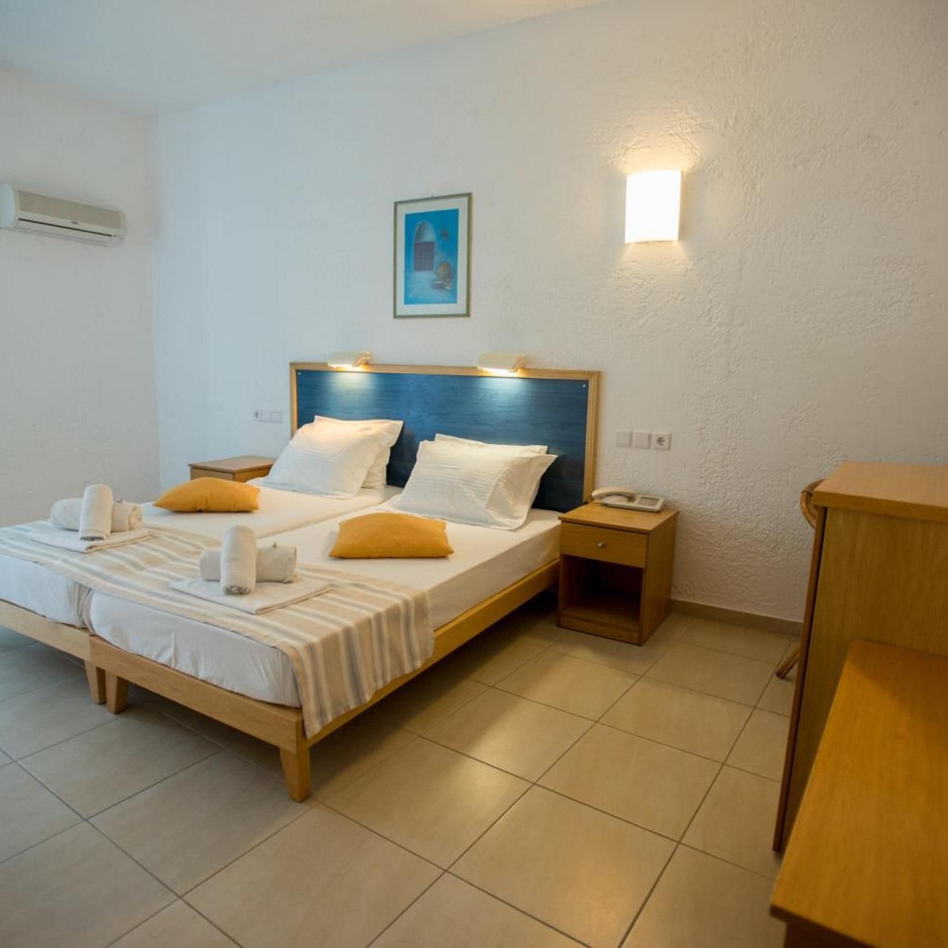 A hotel room with a bed, bedside tables, a bedside lamp, a wall-mounted light, and a painting.