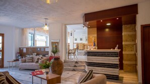 A hotel lobby with a reception desk, seating area, and a staircase leading to other floors. - Neos Ikaros (Agios Vasileios)