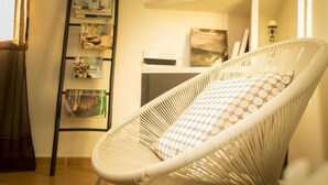 Una cadira de vimet blanc amb un coixí de punts i una habitació amb una prestatgeria i una taula petita.
