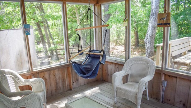 Eine Holzhütte mit einem Hängesessel, zwei Korbstühlen und einem kleinen Tisch.