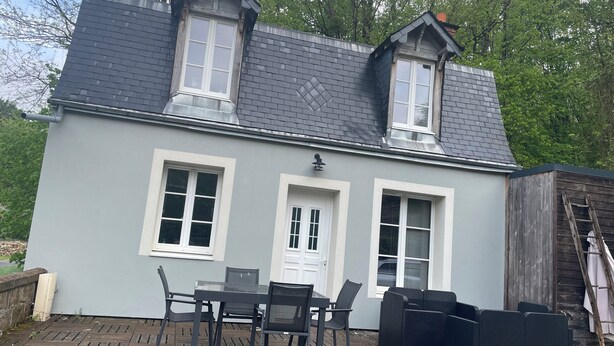 A two-story house with a grey exterior, a dark roof, and a small porch area with a table and chairs.