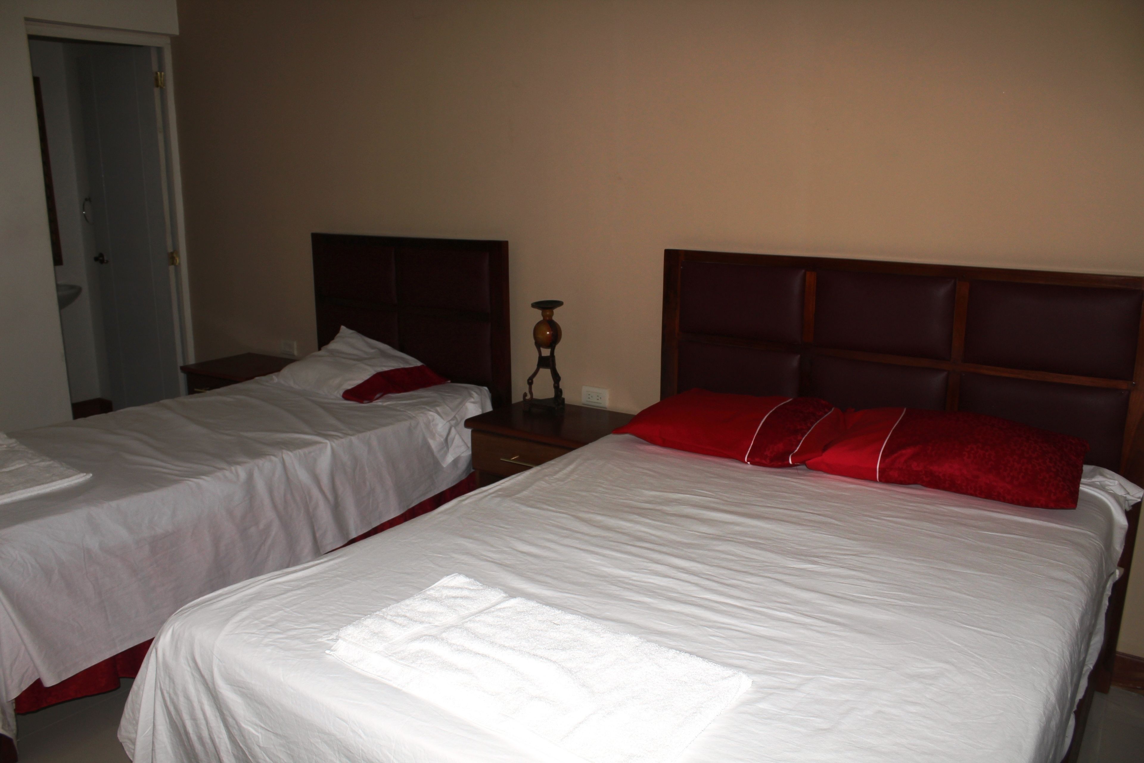 Dos camas individuales con cabeceros de madera, ropa de cama blanca y almohadas rojas en una habitación con paredes color crema.