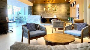 A hotel lobby with a reception desk, seating area with chairs and a round table, and a large window providing a view of the outdoors.