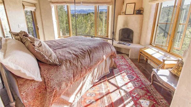 A bedroom with a large bed, a fireplace, and multiple windows offering a view of the outdoors. - Luxury Guesthouse w Views, Private Sauna & Hot Tub- 30 day minimum. (Santa Fe)