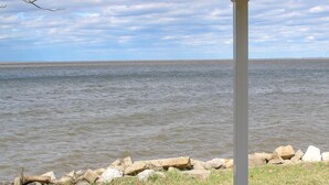 Terraza de madera techada con vista al mar, pilares blancos y un ventilador de techo.