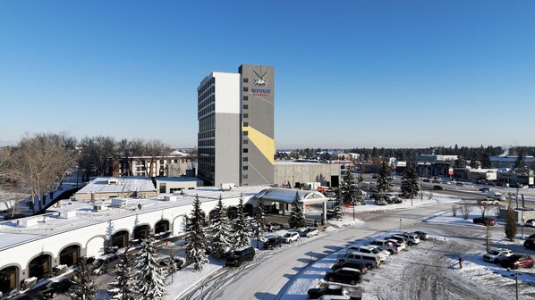 A tall building with a distinctive logo and signage, surrounded by a parking lot and snow-covered trees.