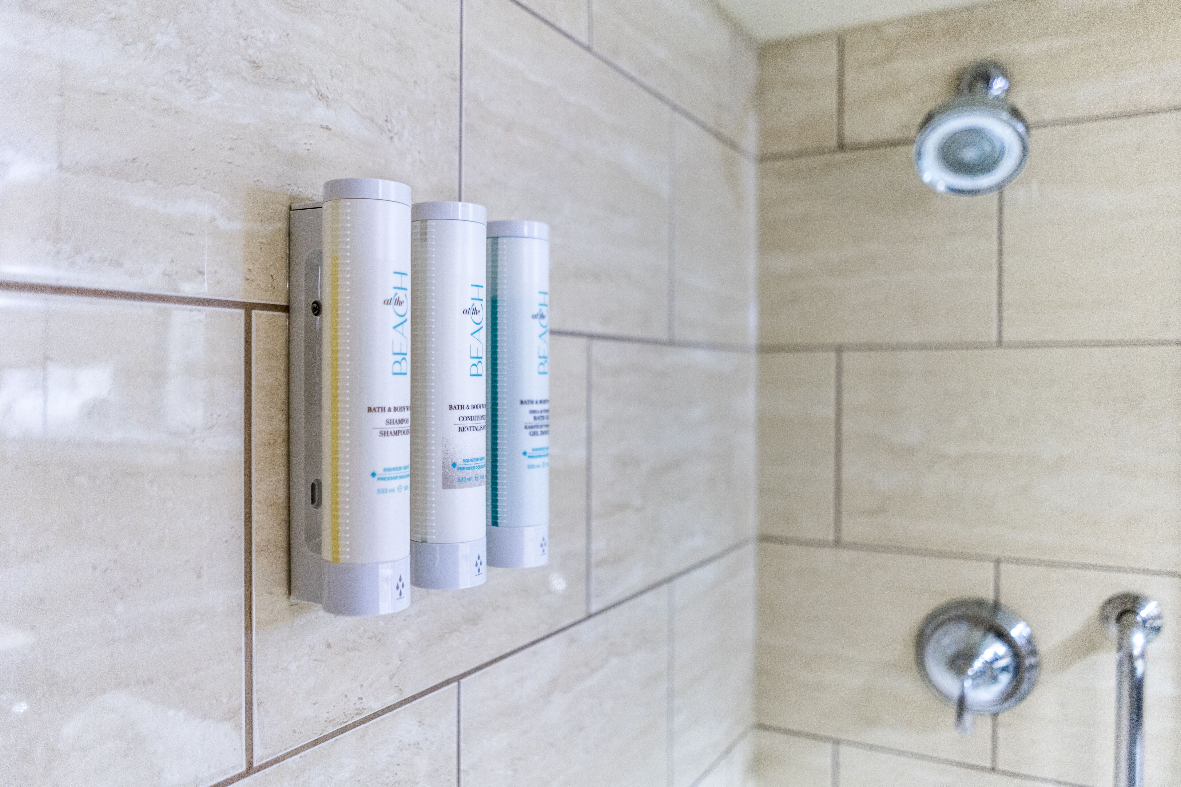 A bathroom with three bottles of bath products on a tiled wall.