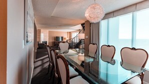 Un comedor moderno con una mesa de vidrio y sillas acolchadas, una lámpara decorativa y vistas al exterior.