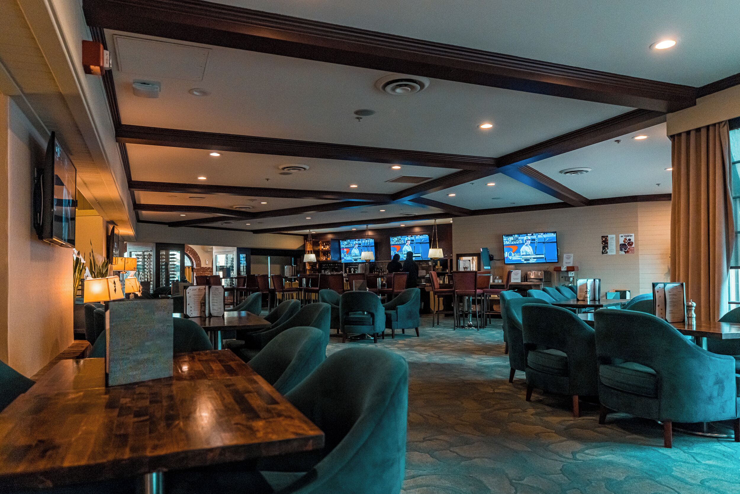 A hotel lobby with multiple seating areas, a bar, and several televisions displaying content.