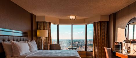 A hotel room with a large bed, a desk, and a view of a cityscape.