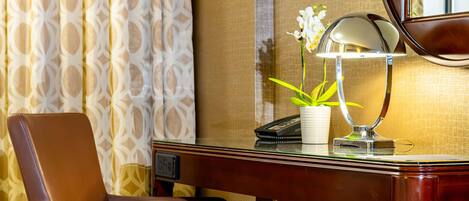 A hotel room with a leather chair, a desk with a lamp, a potted plant, and a telephone.