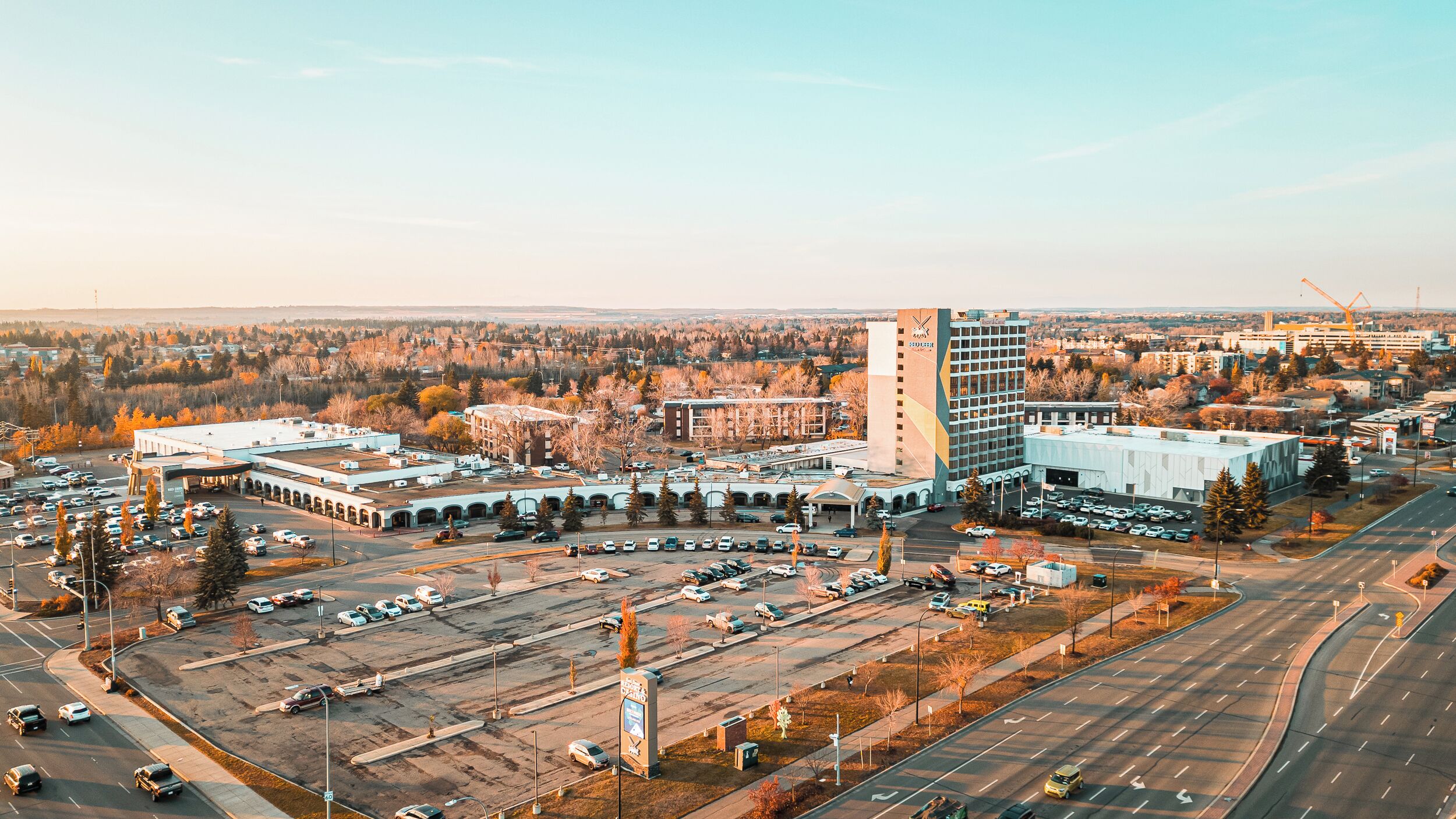 An aerial view of a cityscape with a prominent building featuring a tall tower, a parking lot, and surrounding urban infrastructure.