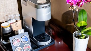 A coffee machine with a tray of coffee pods, a cup of coffee, and a potted orchid on a wooden surface.