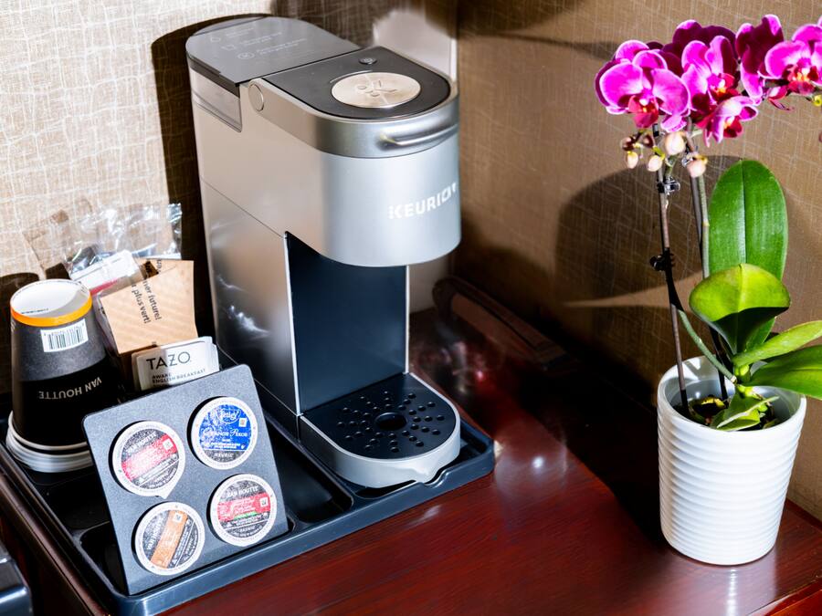 A coffee machine with a tray of coffee pods, a cup of coffee, and a potted orchid on a wooden surface.