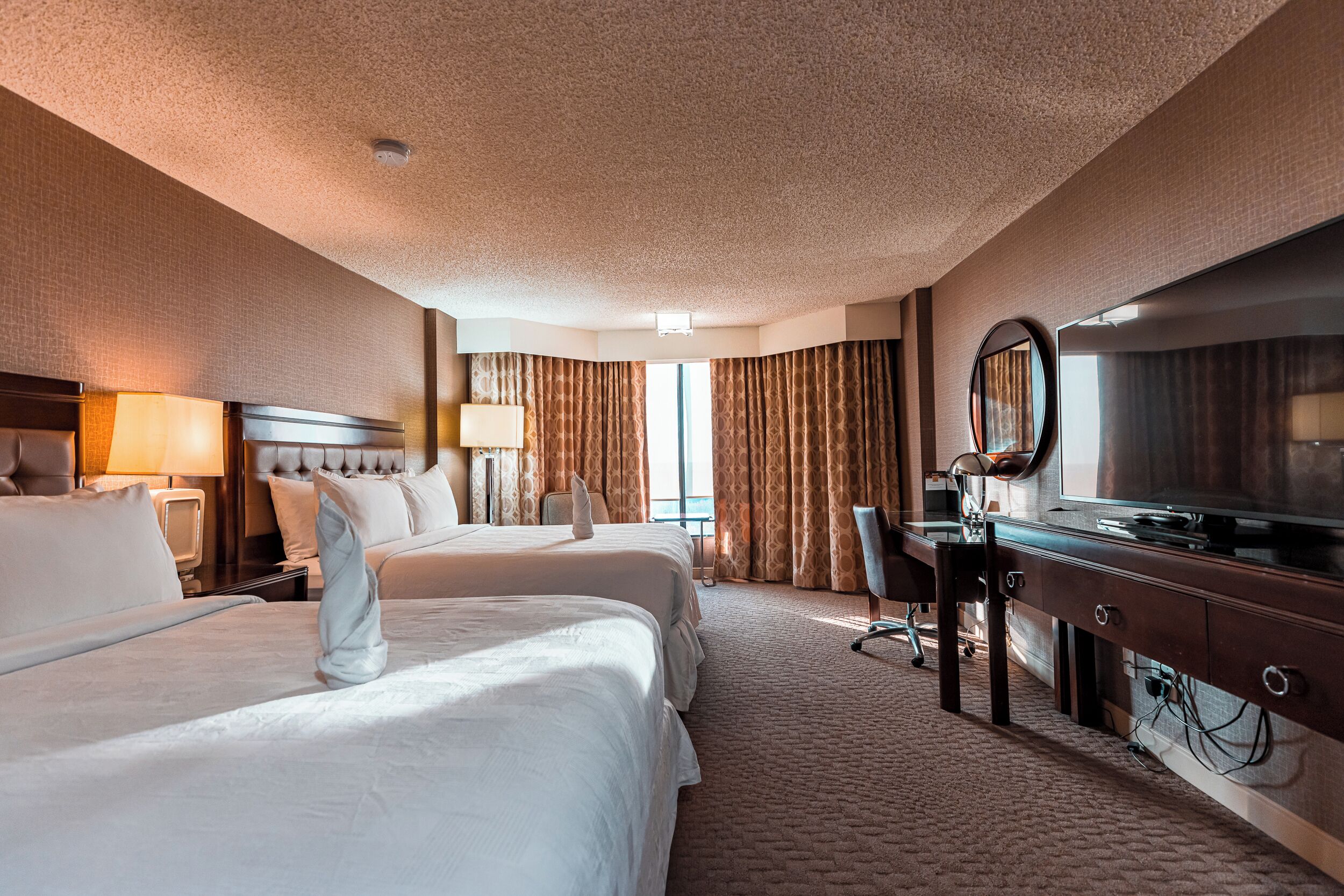 A hotel room with two beds, a desk, a chair, a TV, and a large mirror.