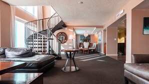 Un espacio habitable amplio con una escalera moderna, sofás de cuero, una mesa de centro redonda y un comedor con sillas y una lámpara.