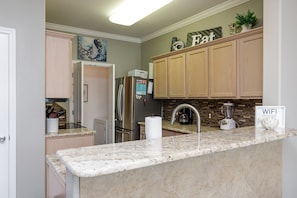 A modern kitchen with granite countertops, wooden cabinets, a refrigerator, and a coffee maker.