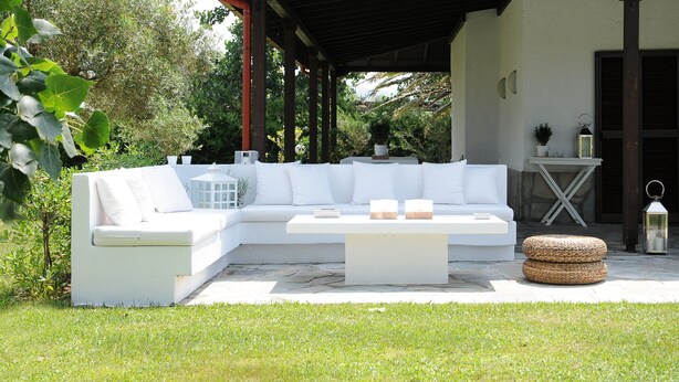 Un divano angolare bianco con un tavolino da caffè abbinato, un poggiapiedi in vimini e una lanterna su un patio in pietra.