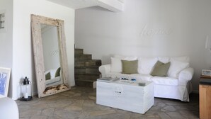 Un soggiorno bianco con un divano bianco, un settimino bianco, uno specchio rustico e una scala.