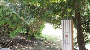 Una struttura in legno con una porta metallica, uno sgabello di vimini e un sentiero in pietra.
