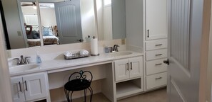 A bathroom with a white sink, a mirror, a towel rack, and a black chair.