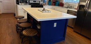 A kitchen with a central island, bar stools, a microwave, a coffee maker, and a refrigerator.