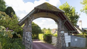 A stone archway leading to a gated area with a wooden fence and a signboard.
