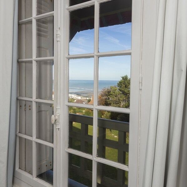 A view through a window with a white frame and multiple panes, overlooking a beach and a residential area. - The beach in Normandy (Hautot sur mer)