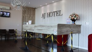 Un mostrador de recepción en el Hotel AJ con una pared de diseño greca, una araña y una silla roja.