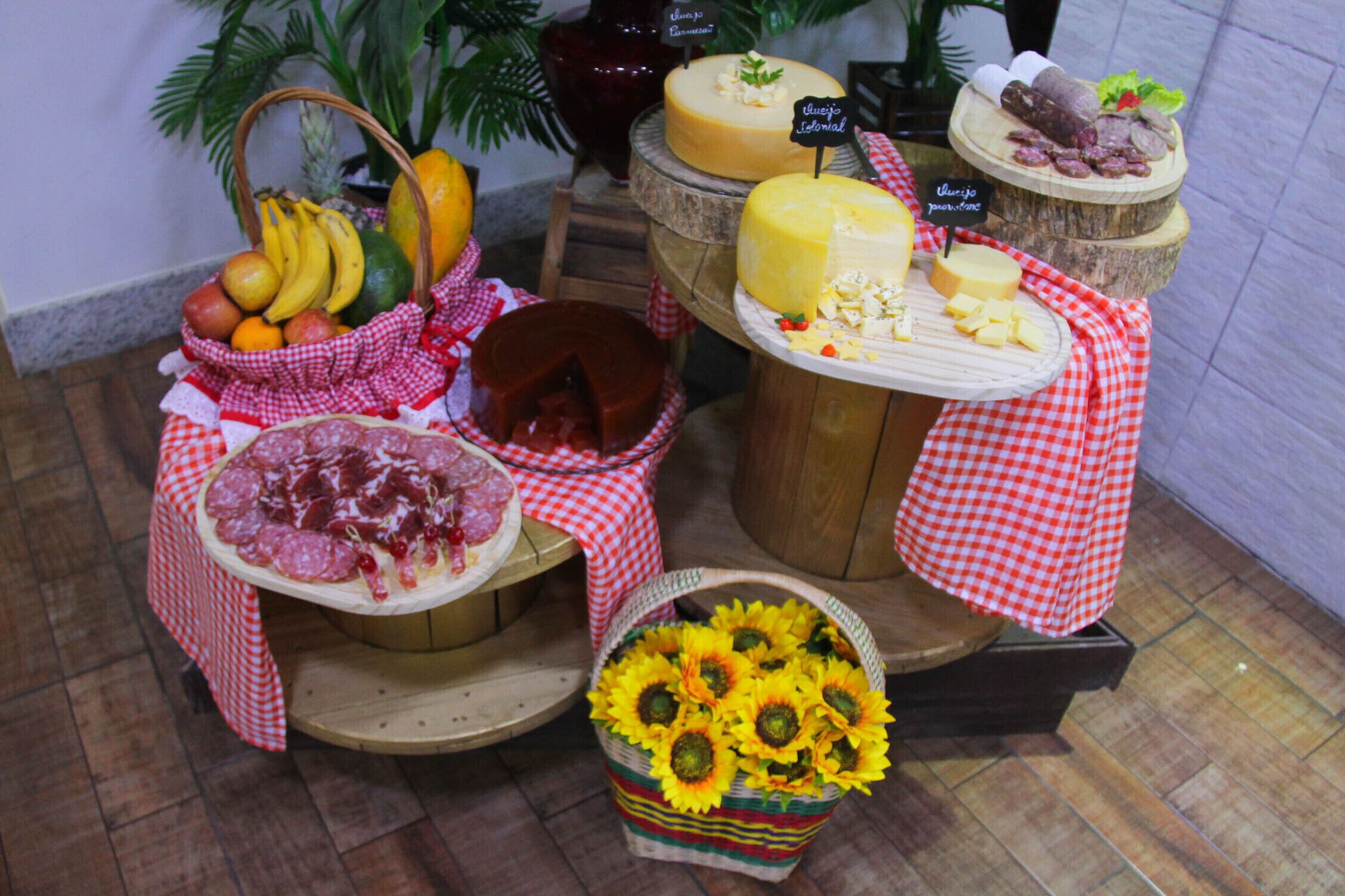 Esposizione di formaggi e frutta con diversi tipi di formaggio e frutta su supporti in legno, il tutto circondato da una tovaglia a quadri.