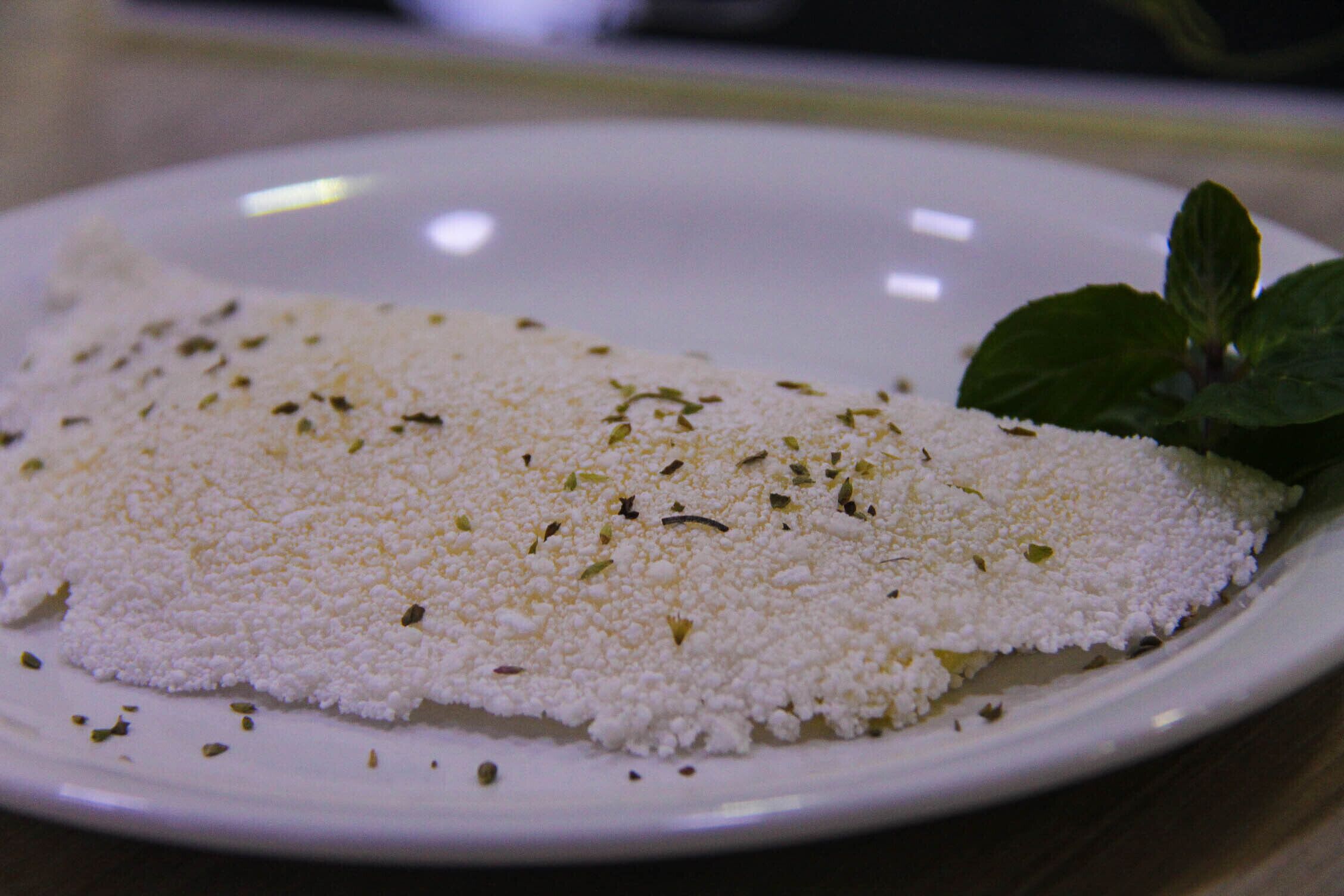 Un plato blanco con un alimento blanco, posiblemente queso, decorado con hierbas.