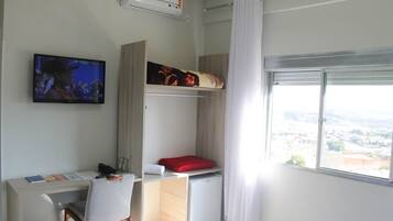 A compact hotel room with a bunk bed, a desk with a chair, a television, and a window with a city view.